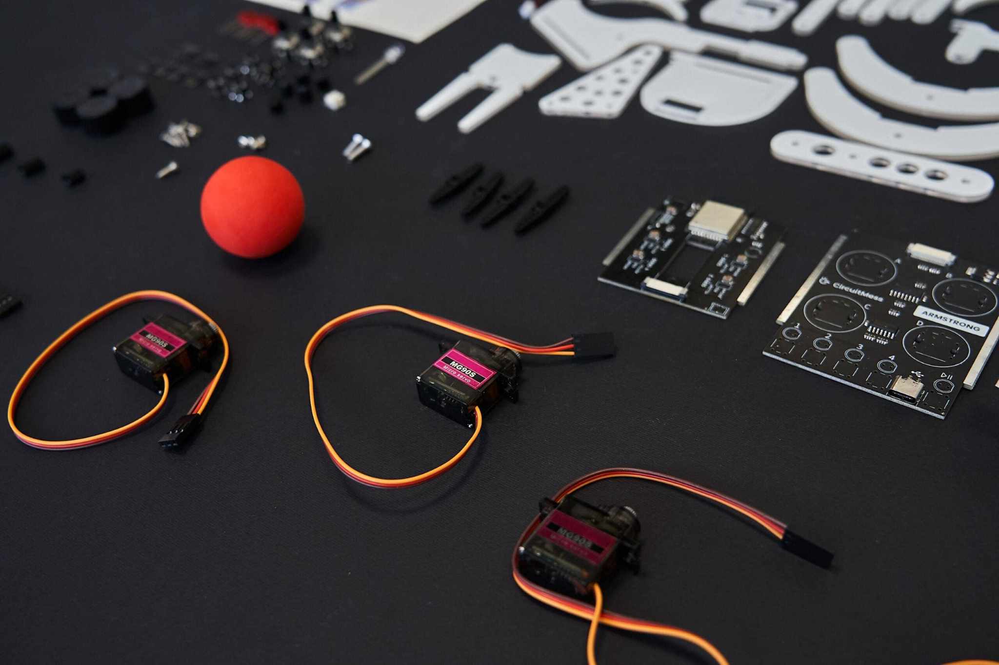DIY Color Detecting Armstrong robotic arm kit parts including servo motors, circuit boards, and a red ball on black background