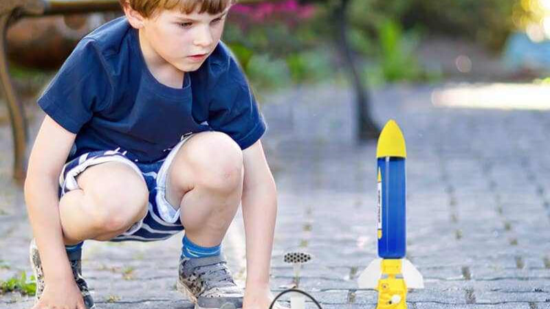 Child playing with a blue and yellow water powered rocket set outdoors on a paved surface