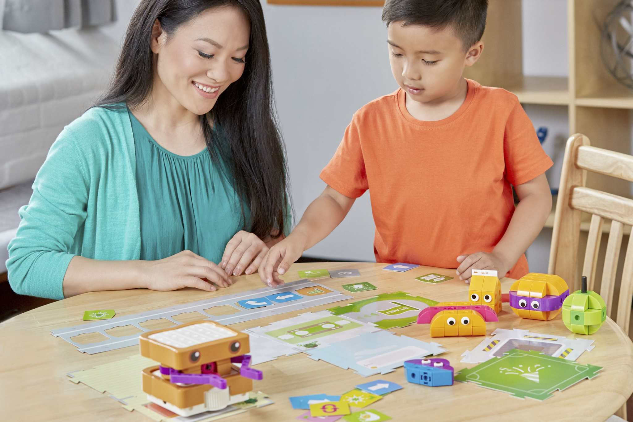 Mother and son playing with Kids First coding and robotics educational toy on a table with colorful coding cards and robot models.