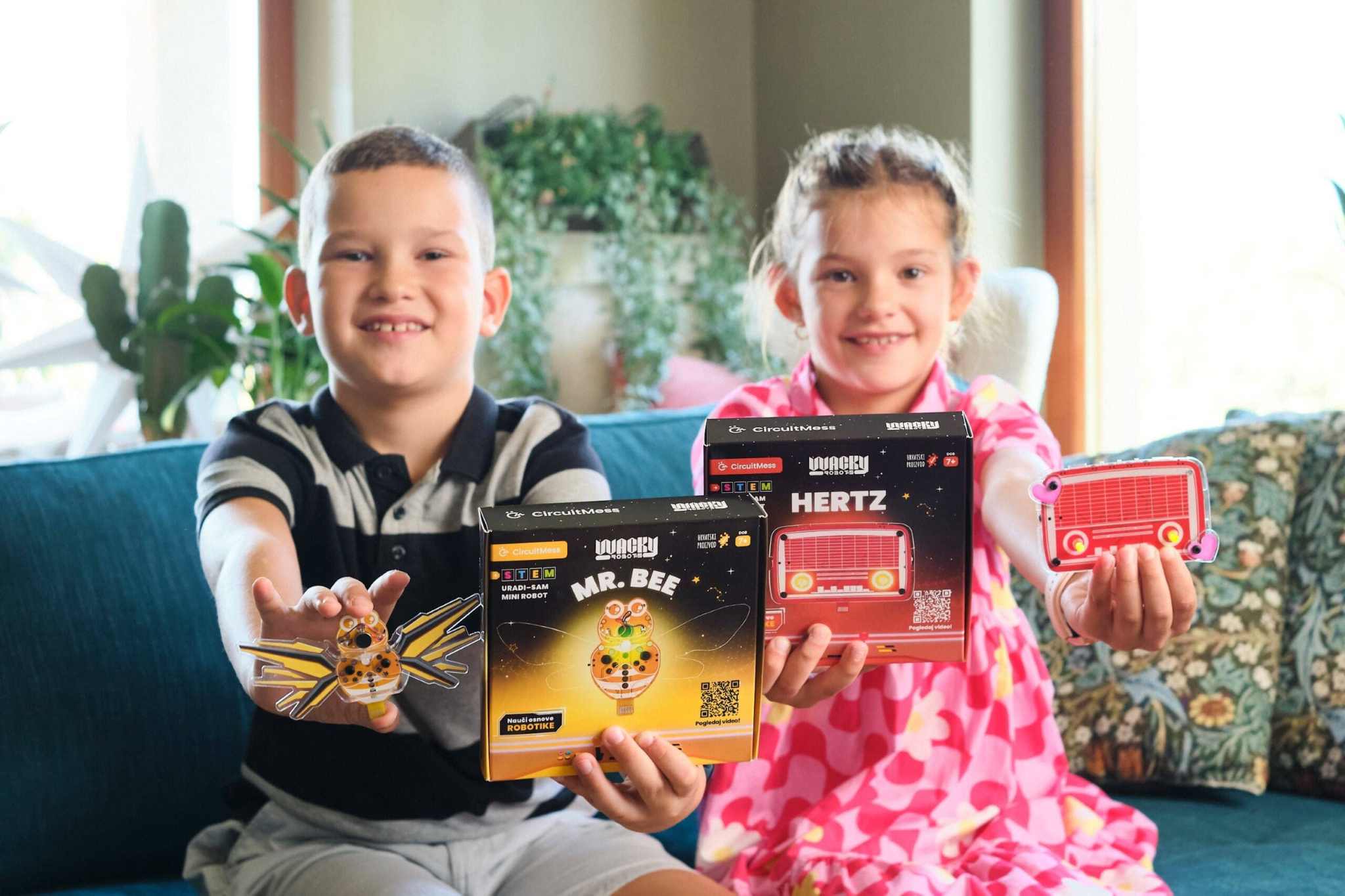 Children holding Wacky Robot Hertz mini robot kit and finished blinking robot toy on a couch