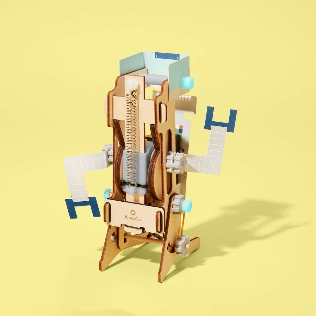 Wooden jumping robot model with spring mechanism and blue motor parts on yellow background