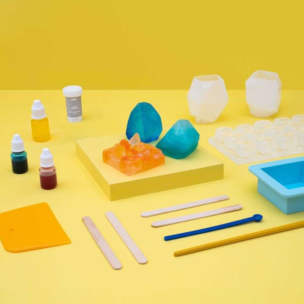 Crystal Geode Soapmaking Kit with silicone molds, liquid colors, mica powder, and craft sticks on yellow background
