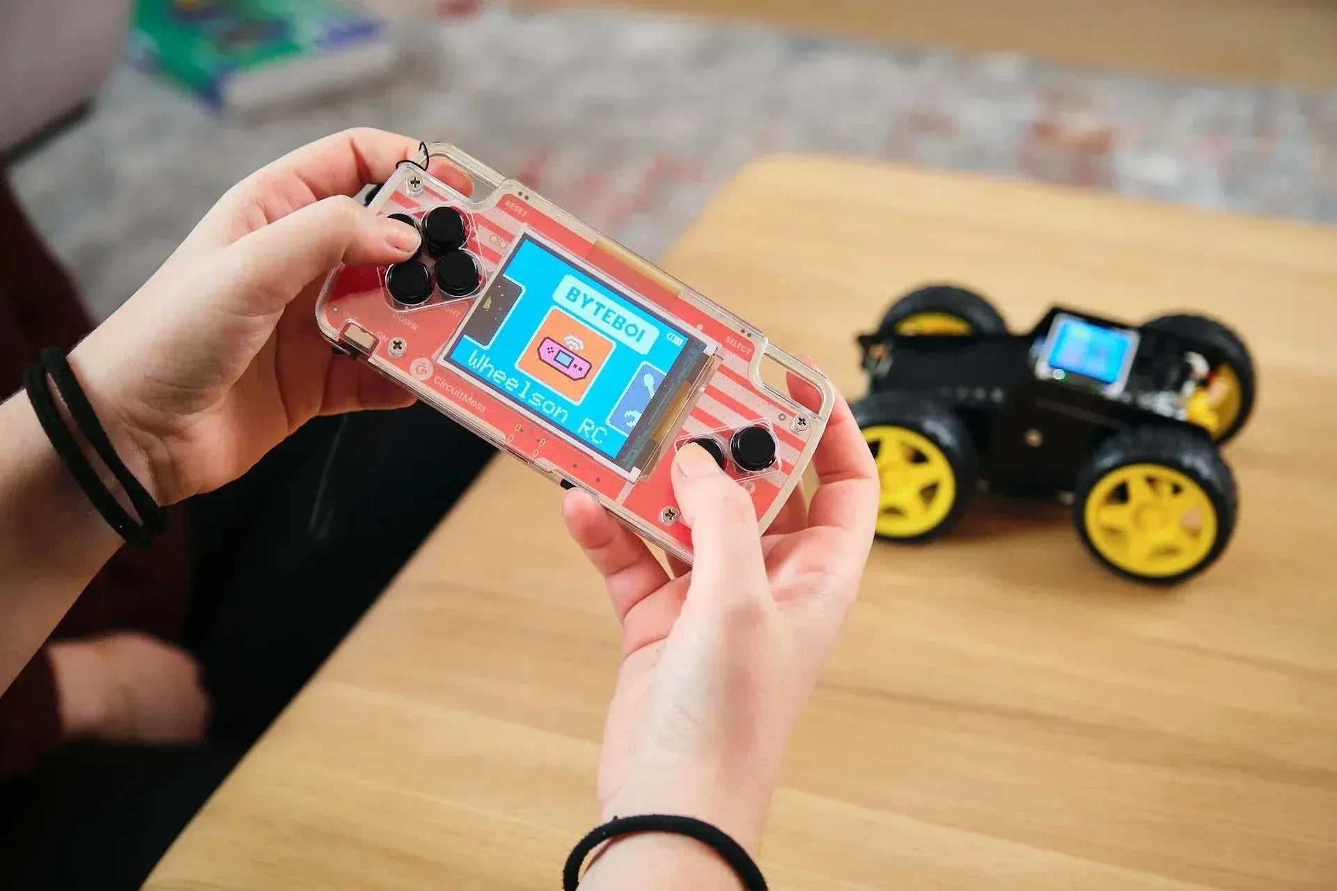 Hands holding a transparent remote control for Wheelson AI-powered self-driving robot car with the car blurred on a wooden table background