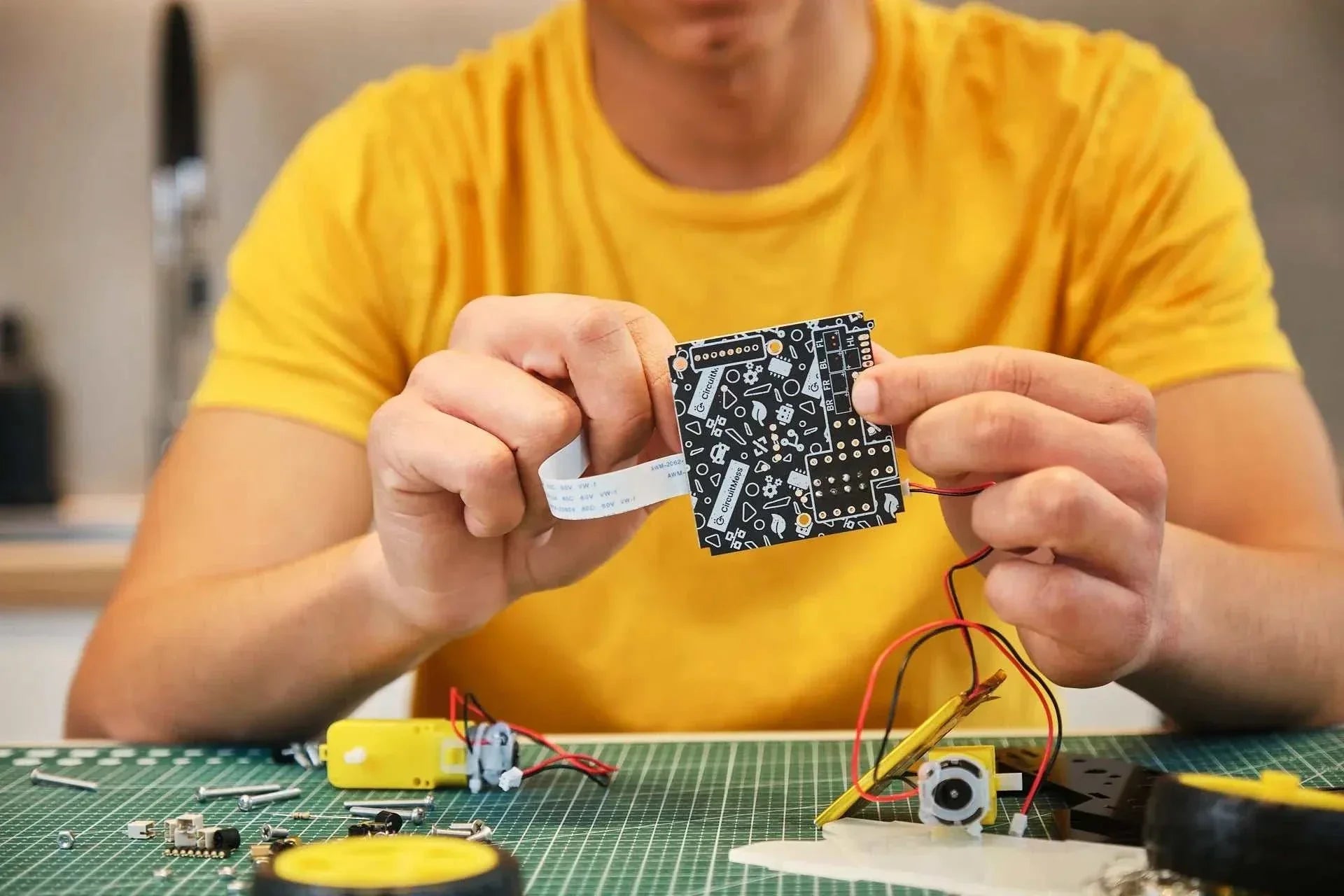 Person assembling circuit board for Wheelson AI-powered self-driving robot car kit with wires and components on workbench.