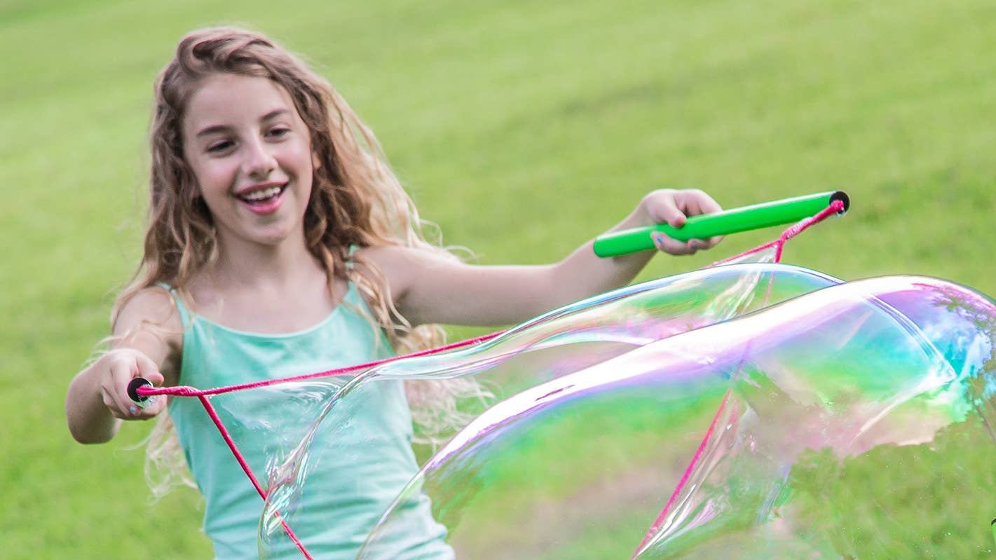 Girl using WOWmazing Giant Bubble Kit to create large colorful bubbles outdoors