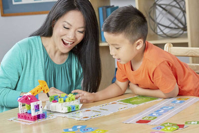 Mother and son playing with Kids First coding and robotics educational kit on table with colorful building blocks and coding cards.