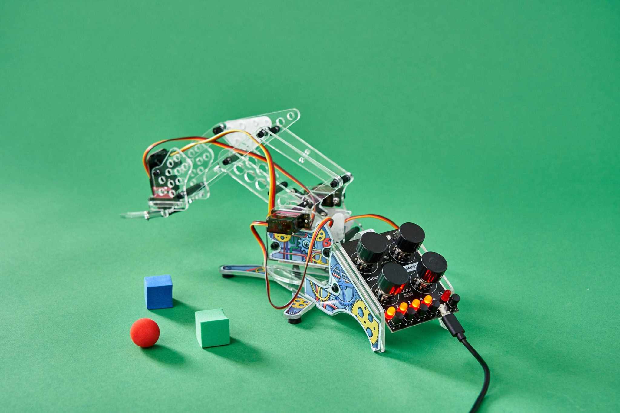 DIY color detecting robotic arm with sensors, wires, and colorful blocks on a green background.