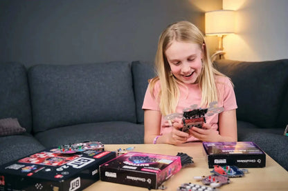 Girl assembling Wacky Robot Artemis mini robot kit with electronics and LED components on table.