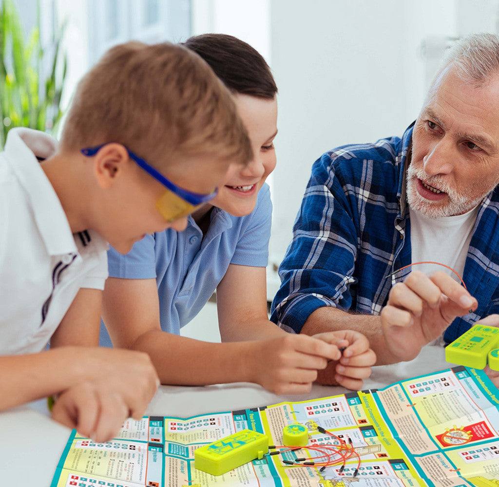 Children and an adult assembling Tiny Circuits mini-microprocessor electronics kit with wires and instructions.