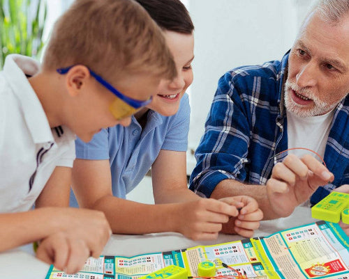 Children and an adult assembling Tiny Circuits mini-microprocessor electronics kit with wires and instructions.